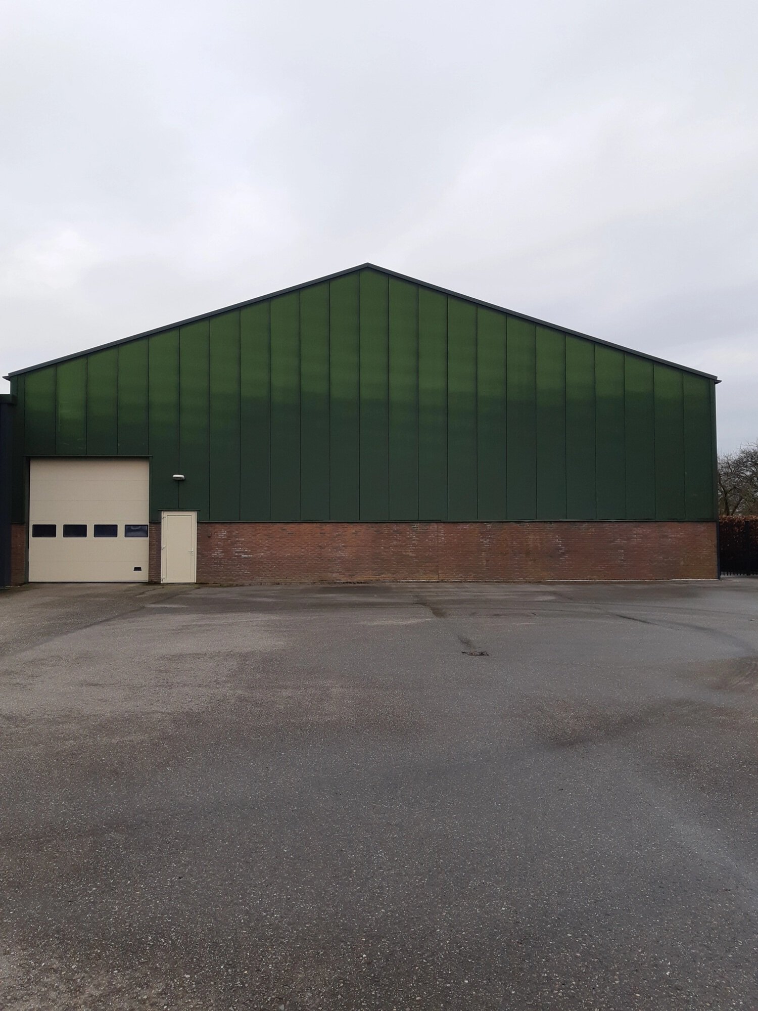 Groene industriële hal met bakstenen onderkant en grote garagepoort.