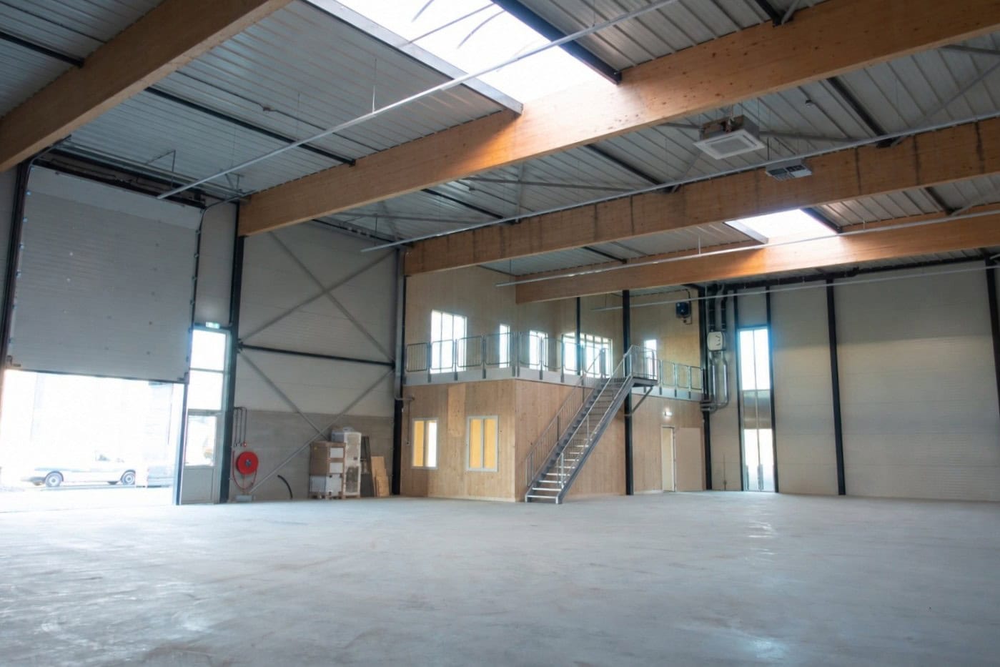 Ruime industriële hal met verhoogde kantoorruimte en grote overheaddeur.