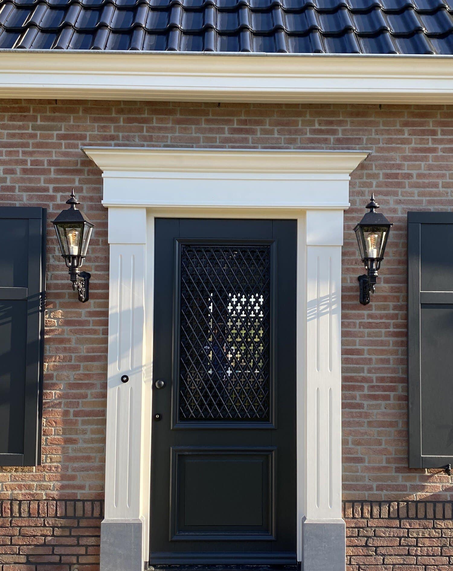 Voordeur van een notariswoning met klassieke witte omlijsting en zwarte lampen.